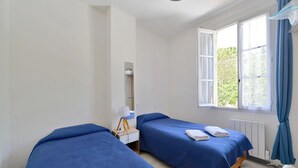 Una habitación con dos camas, una mesita de noche pequeña, una lámpara y una ventana con cortinas.