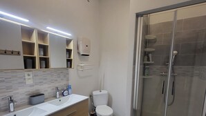 Un baño moderno con cabina de ducha de vidrio, inodoro blanco y tocador con espejo y estantes.
