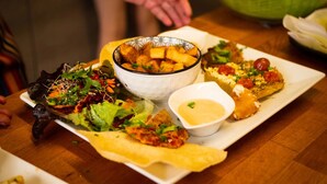 Una mesa con varios platos, incluyendo una ensalada, papas fritas y un platillo empanizado, además de un tazón de papas fritas y un recipiente pequeño de salsa.