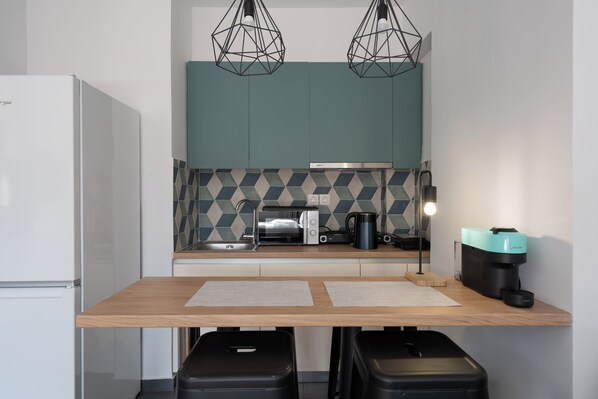A compact kitchen with a refrigerator, microwave, toaster, coffee maker, and a wooden table with two stools. - Orion Stunning Studio in Athens (Athens)