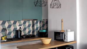 Eine moderne Küche mit türkisfarbenen Schränken, einer geometrischen Spritzschutzwand, einem Holztisch, einer Mikrowelle und einer Kaffeemaschine.