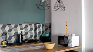 Una cocina moderna con armarios verde azulado, un salpicadero geométrico, una mesa de comedor de madera, un microondas y una cafetera.