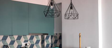 A modern kitchen with teal cabinets, a geometric backsplash, a wooden dining table, a microwave, and a coffee maker.