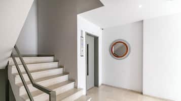 Un interior moderno con una escalera, un ascensor y un espejo circular en la pared.