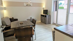 A modern kitchen with a dining area, a TV on a wooden cabinet, and a sliding glass door leading to a balcony. - Comfortable, fully equipped apartments, near Geesthacht  (Geesthacht)