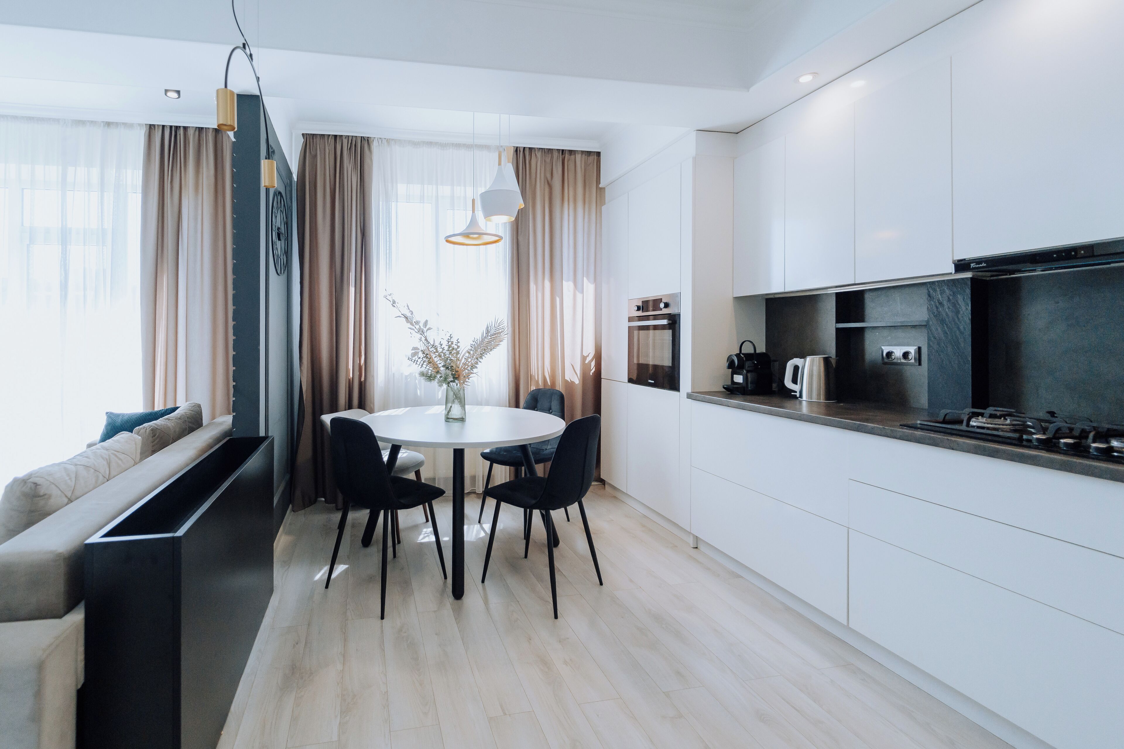A modern kitchen with white cabinets, a dining area with a round table and chairs, and a built-in oven.