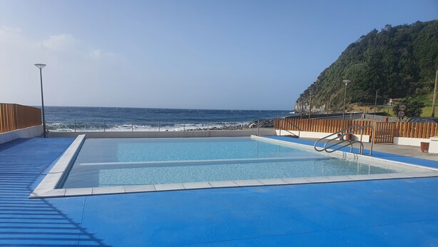 A pool with a view of the ocean and a wooden deck.