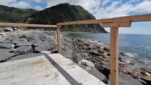 A wooden pier leading to a rocky beach with a mountain in the background.