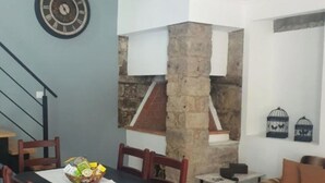 A dining area with a table, chairs, a basket of food, a clock on the wall, and a stone pillar.