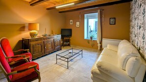 Un salon avec un plafond en bois, un canapé blanc, un fauteuil rouge, une télévision et un meuble.