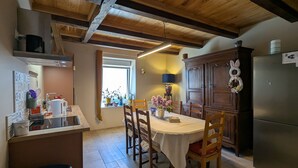 Une cuisine avec des poutres en bois, une table à manger avec des chaises, un réfrigérateur et une fenêtre ornée de plantes.