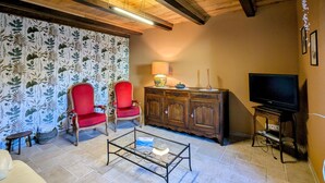 Un salon avec des poutres apparentes en bois au plafond, un téléviseur, un meuble et deux fauteuils rouges.