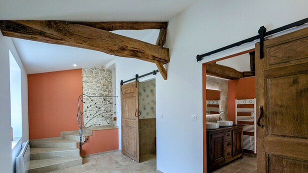 Un escalier mène à une pièce dont un des murs est en pierre, qui possède une porte en bois et comprend un coin cuisine avec un porte-serviettes blanc.