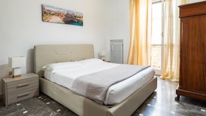 Une chambre à coucher comprenant un lit, des tables de chevet, un radiateur, une armoire en bois et une fenêtre avec des rideaux.