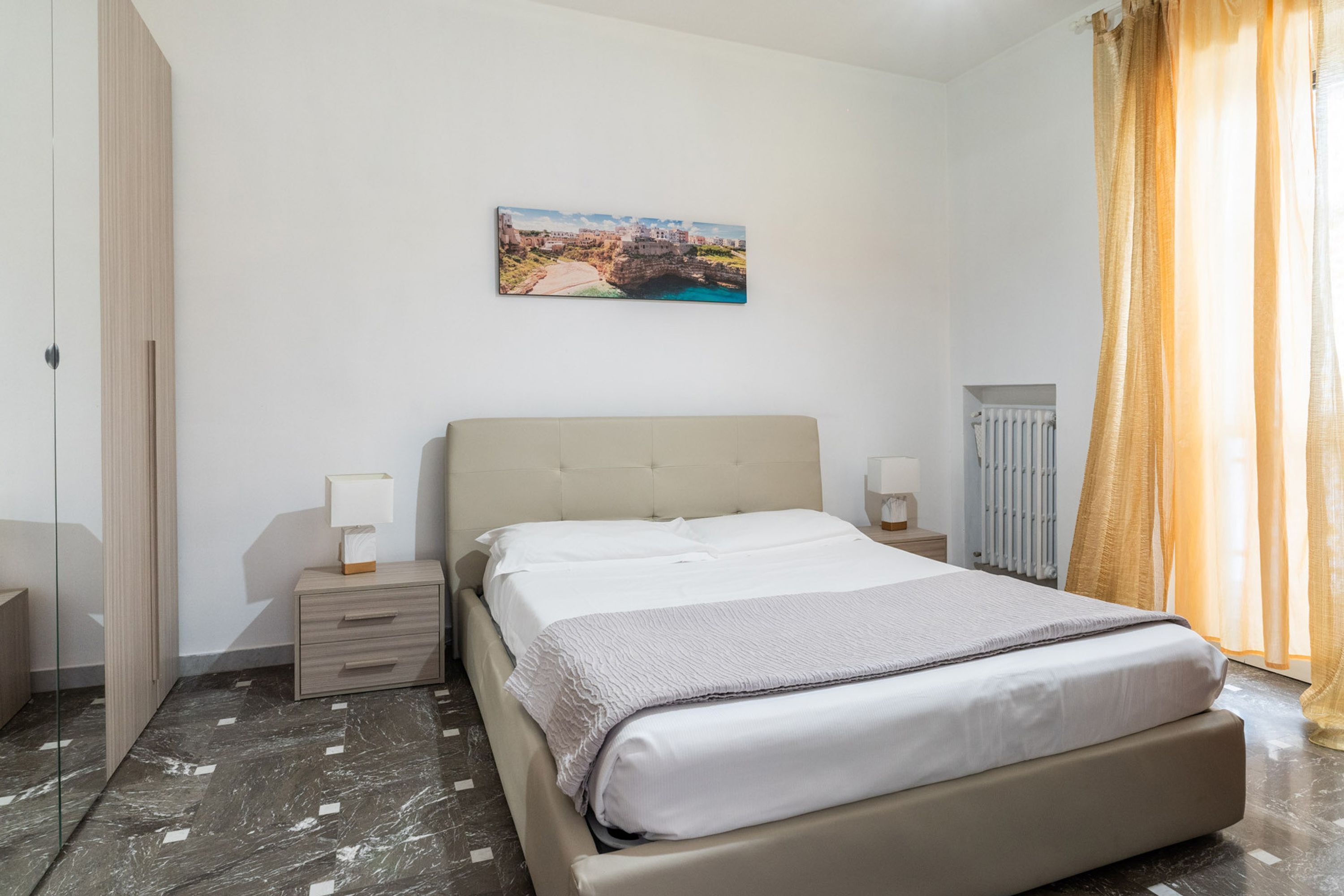 Une chambre à coucher avec un lit, des tables de chevet, un radiateur et un tableau au mur.