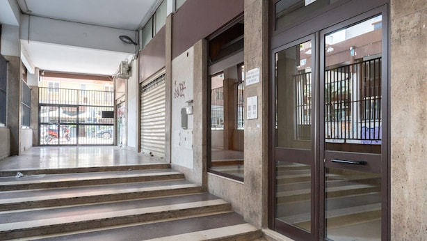 L’entrée d’un immeuble, avec un escalier en béton menant à une porte en verre.