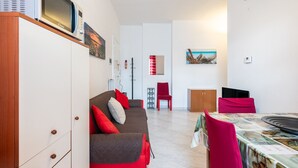 Un salon moderne avec un canapé, des fauteuils rouges, une table à manger et un four à micro-ondes fixé au mur.