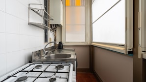 Une cuisine de taille réduite, équipée d’une cuisinière à gaz, d’un évier et d’une fenêtre.
