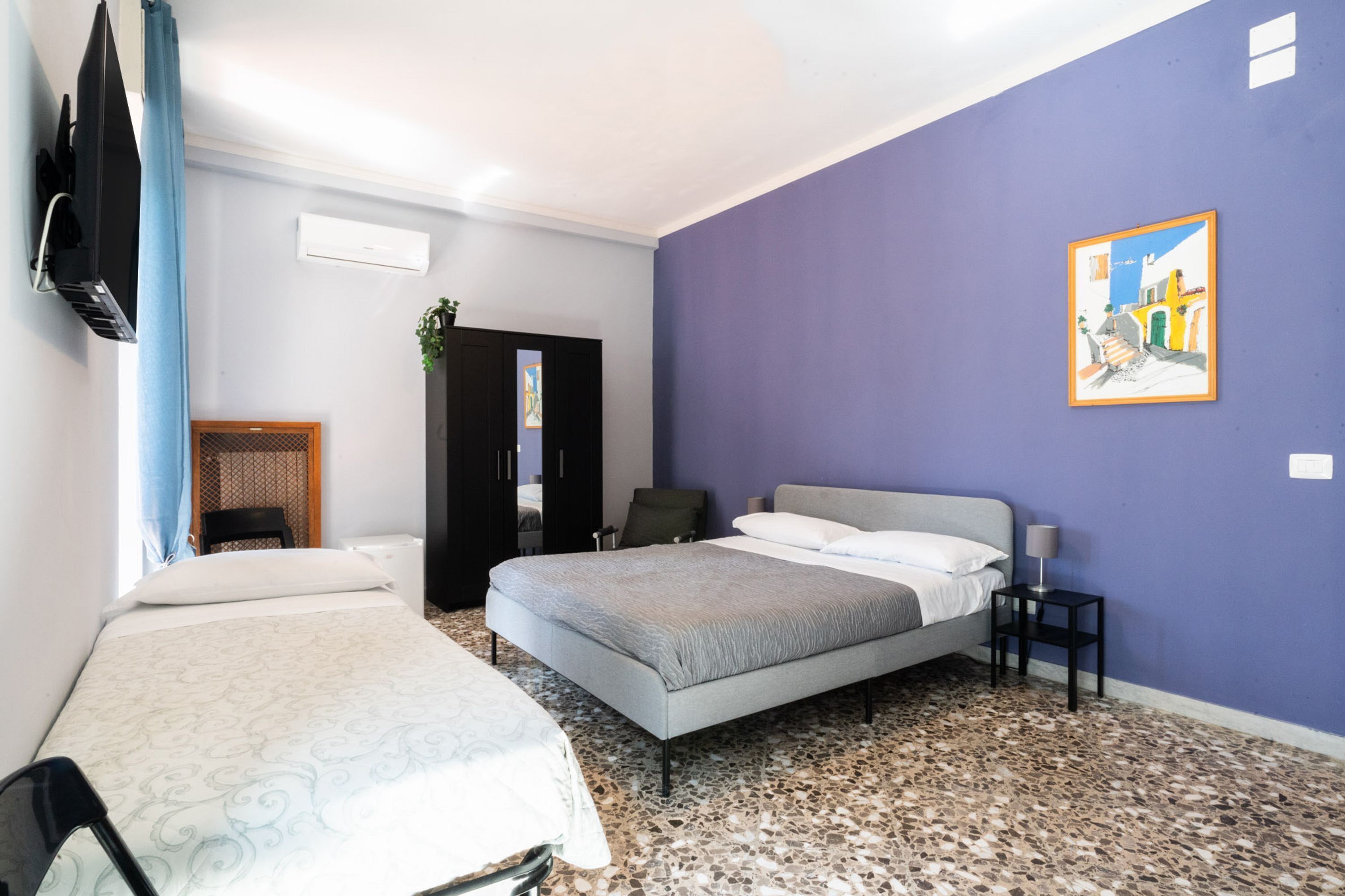 A hotel room with two beds, a TV, a painting, and a door leading to a bathroom.