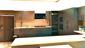 A modern kitchen with dark cabinetry, a central island, and built-in appliances. - Architect-designed house in Nianing Peace and relaxation (NIANING)