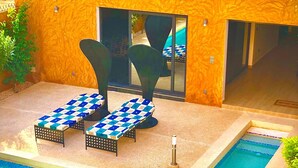 A pool area with a checkered lounge chair set, a pool, and a building with a textured facade. - Architect-designed house in Nianing Peace and relaxation (NIANING)