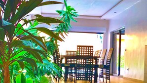 A spacious room with a wooden floor, a dining table with chairs, and lush green plants. - Architect-designed house in Nianing Peace and relaxation (NIANING)