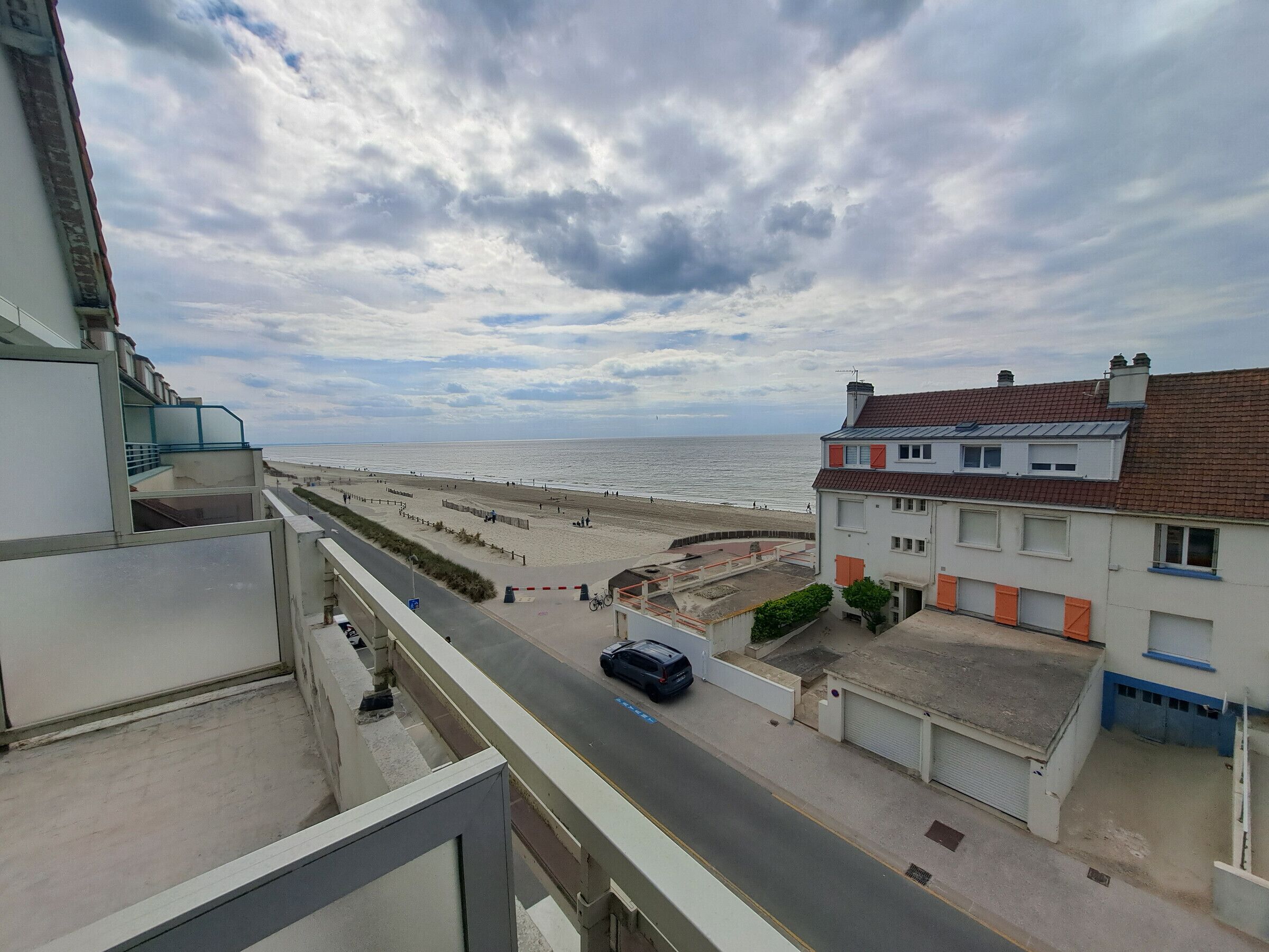 Blick aufs Meer vom Balkon mit Blick auf einen Strand und eine Straße, auf der ein Auto geparkt ist.