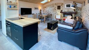 Une cuisine moderne dotée d’un îlot central intégré, un coin repas avec un mur en pierre et un espace salon confortable avec un canapé en cuir.