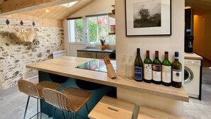 Une cuisine avec un plafond en bois, des murs en pierre, un coin bar avec des chaises en osier et un meuble à vin rempli de bouteilles.