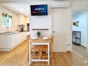 Una cocina moderna con armarios blancos, una mesa de comedor con platos y vasos, y un televisor de pantalla plana montado en la pared que muestra 'SMART TV'.