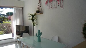 A dining area with a glass table, white chairs, a cactus centerpiece, a TV, and a hanging plant. - Beautiful apartment with terrace for 4 people, near beach in Port Camargue (Port Camargue)