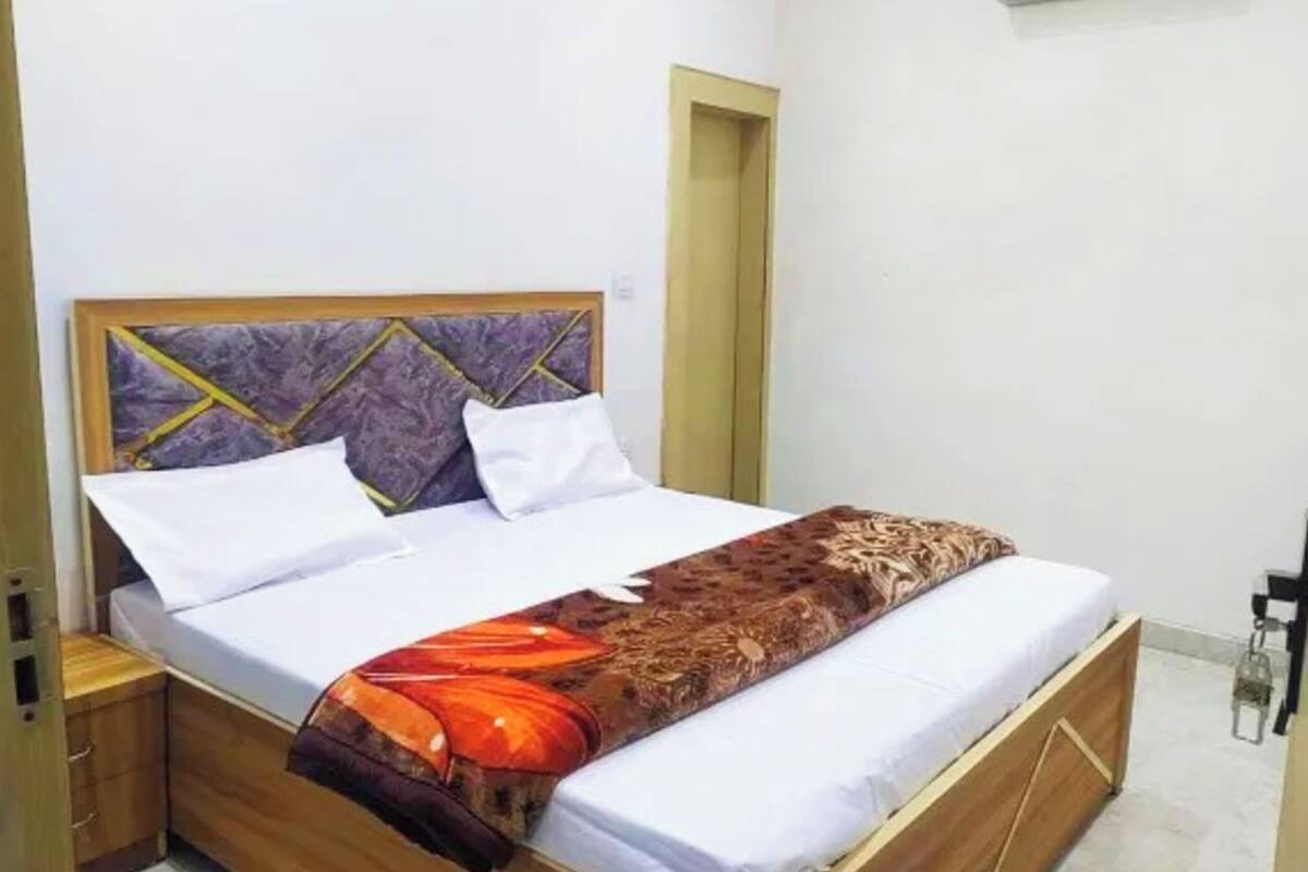 A bed with a patterned headboard, a white pillow, a brown and orange blanket, and a wooden bedside table.