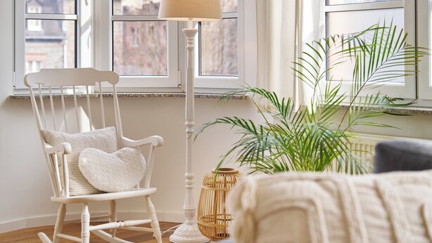 Ein gemütliches Zimmer mit Schaukelstuhl, Stehlampe und Topfpflanze.