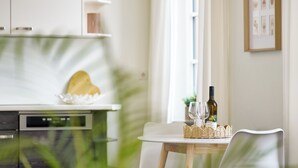 Eine moderne Küche mit weißen Schränken, einer weißen Arbeitsplatte, einem herzenförmigen Holzobjekt und einem Essbereich mit Tisch, Stühlen und einer Weinflasche.