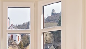 Blick durch ein mehrteiliges Fenster auf eine Kirche, eine Burg auf einem Hügel und eine Stebrücke.