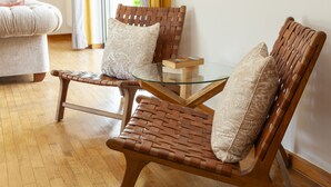 A room with two wicker chairs with cushions, a glass table with a book, and a sofa in the background. - Villa Naturis (Portimão)