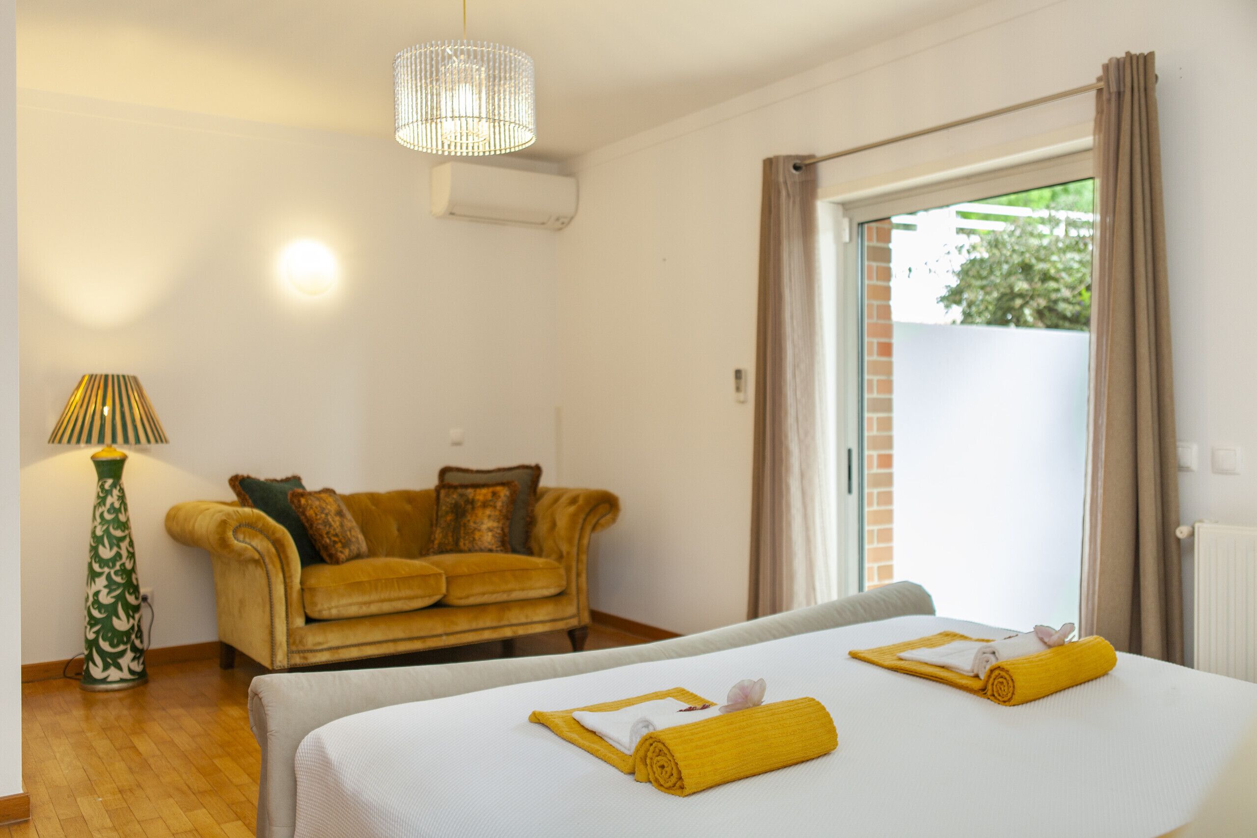 Habitación de hotel con cama, sofá, lámpara y vistas al exterior.