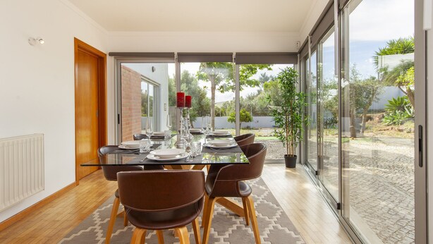 A dining area with a glass table, brown chairs, and a view of the outdoors. - Villa Naturis (Portimão)