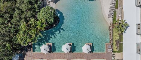 An aerial view of a resort with a clear pool, lounge chairs, and umbrellas.