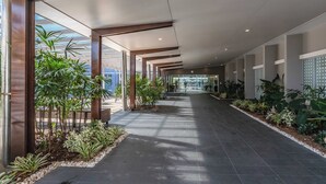Un couloir au design moderne, avec une porte d’entrée en verre, des plantes en pot et un sol carrelé.