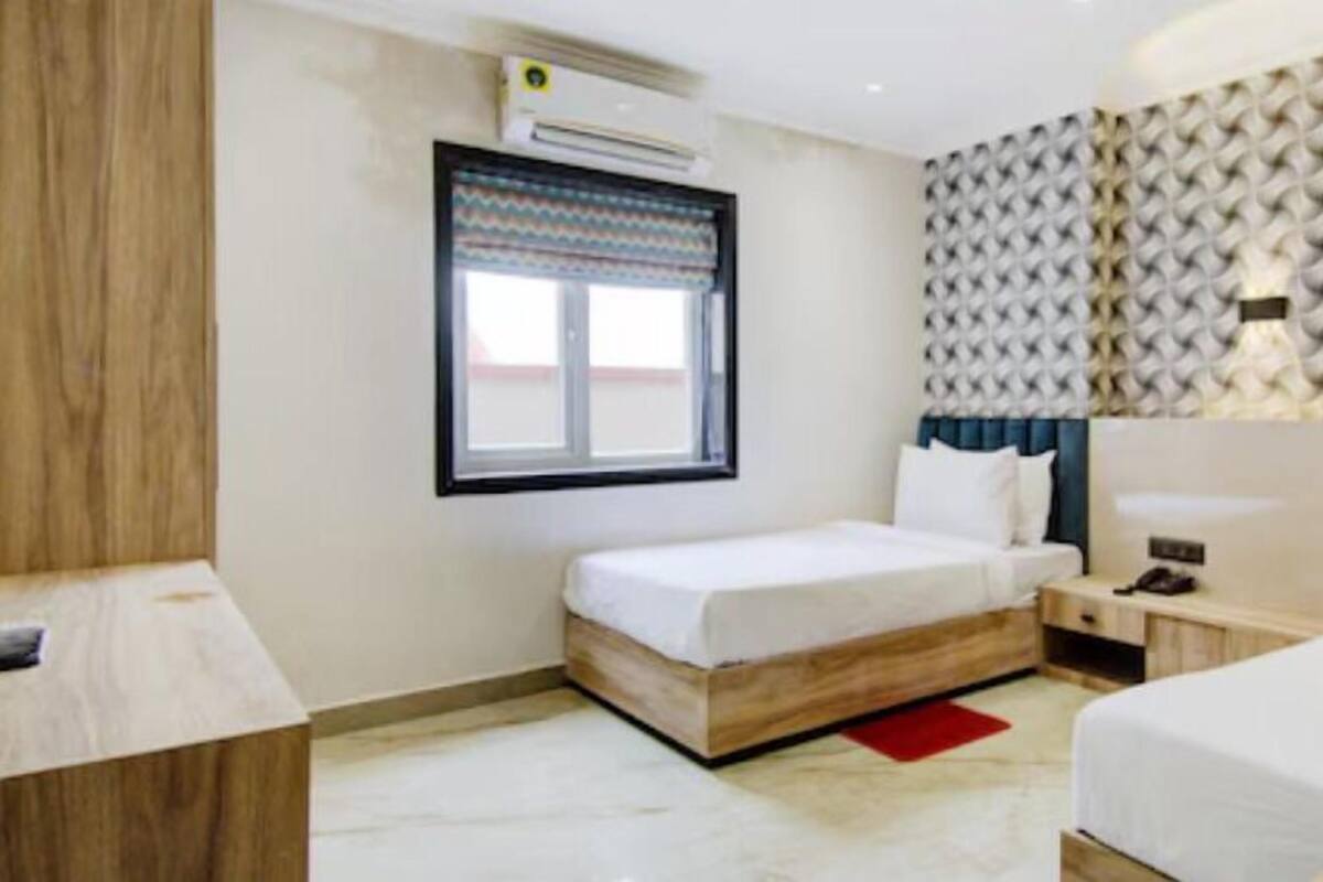 A hotel room with a bed, bedside table, lamp, and a window with a patterned curtain.