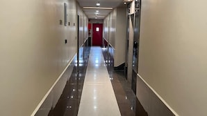Ein langer, schmaler Korridor mit einer roten Tür am Ende, gesäumt von Wänden mit Marmorverkleidung und einer Decke mit Einbauleuchten.