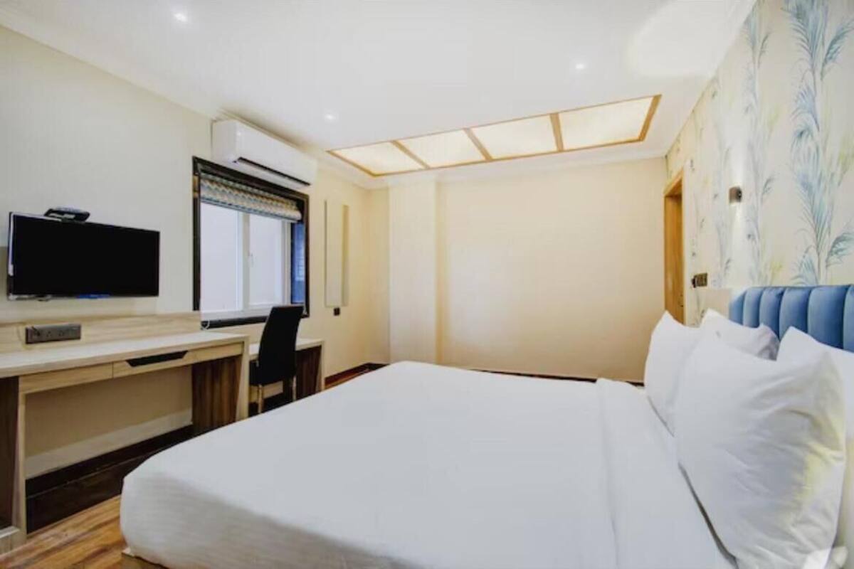 A hotel room with a bed, a desk with a television, and a window with blinds.