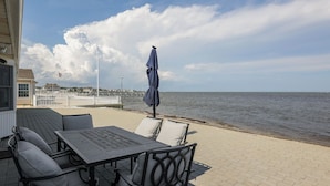 A patio with a table and chairs, overlooking a body of water with a white fence and buildings in the background.
