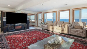 A spacious living room with a large flat-screen TV, a beige sofa set, and a red patterned rug.
