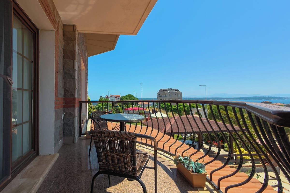 Un balcon avec une table et des chaises, une vue sur la mer et un bâtiment aux murs en pierre et en briques.