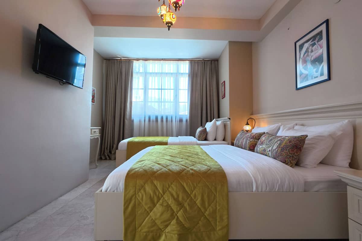 Une chambre d’hôtel avec un grand lit, un téléviseur fixé au mur, une fenêtre avec des rideaux et un lustre.