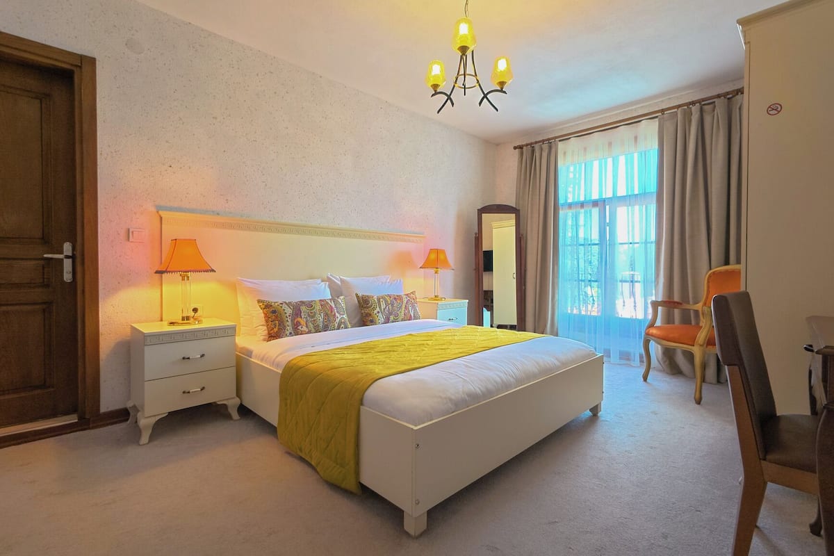 Une chambre à coucher comprenant un lit, deux tables de chevet, une chaise, un bureau, un miroir et un lustre.