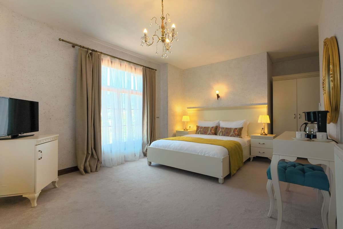 Une chambre d’hôtel avec un lit, des lampes de chevet, un téléviseur posé sur un meuble, un miroir et un lustre.