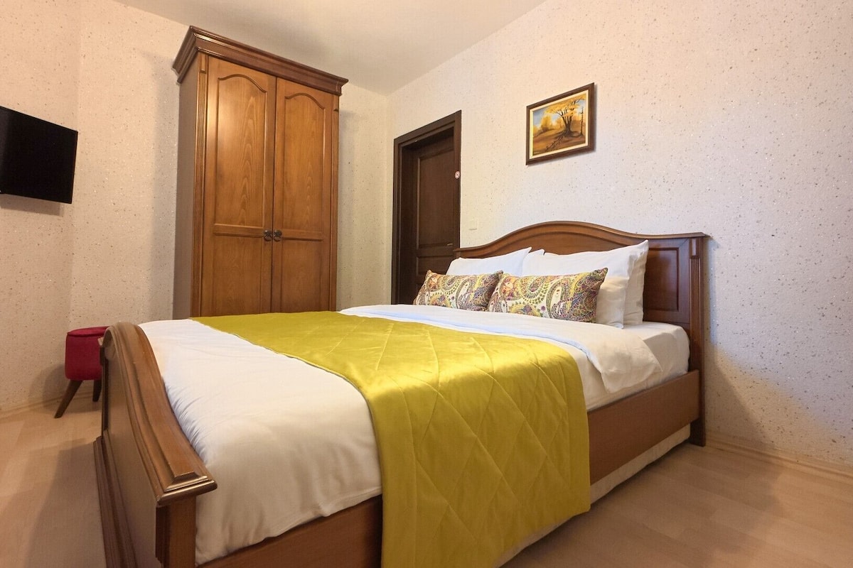 Une chambre à coucher avec un lit, une armoire en bois, une porte, un tableau et un objet rouge sur le sol.